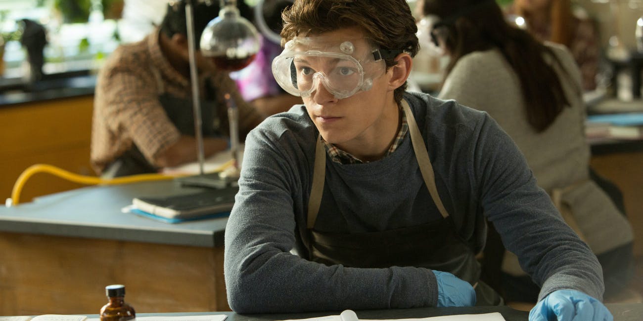 Tom Holland as Peter Parker in science class. He is wearing protective glasses.