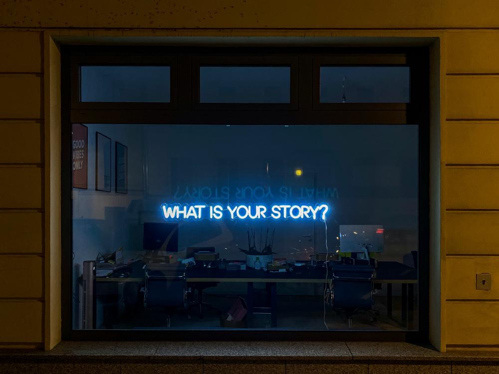 A neon sign reading “What is Your Story"