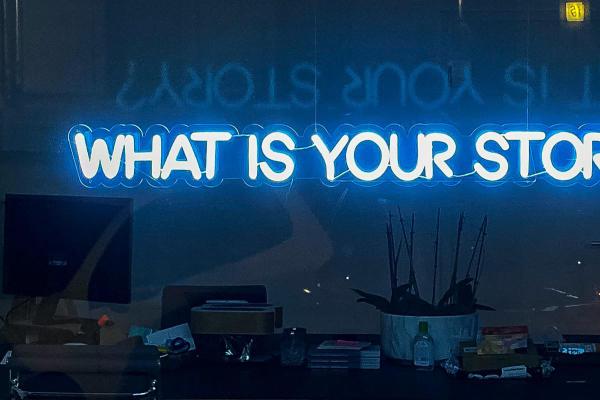 A neon sign reading “What is Your Story"